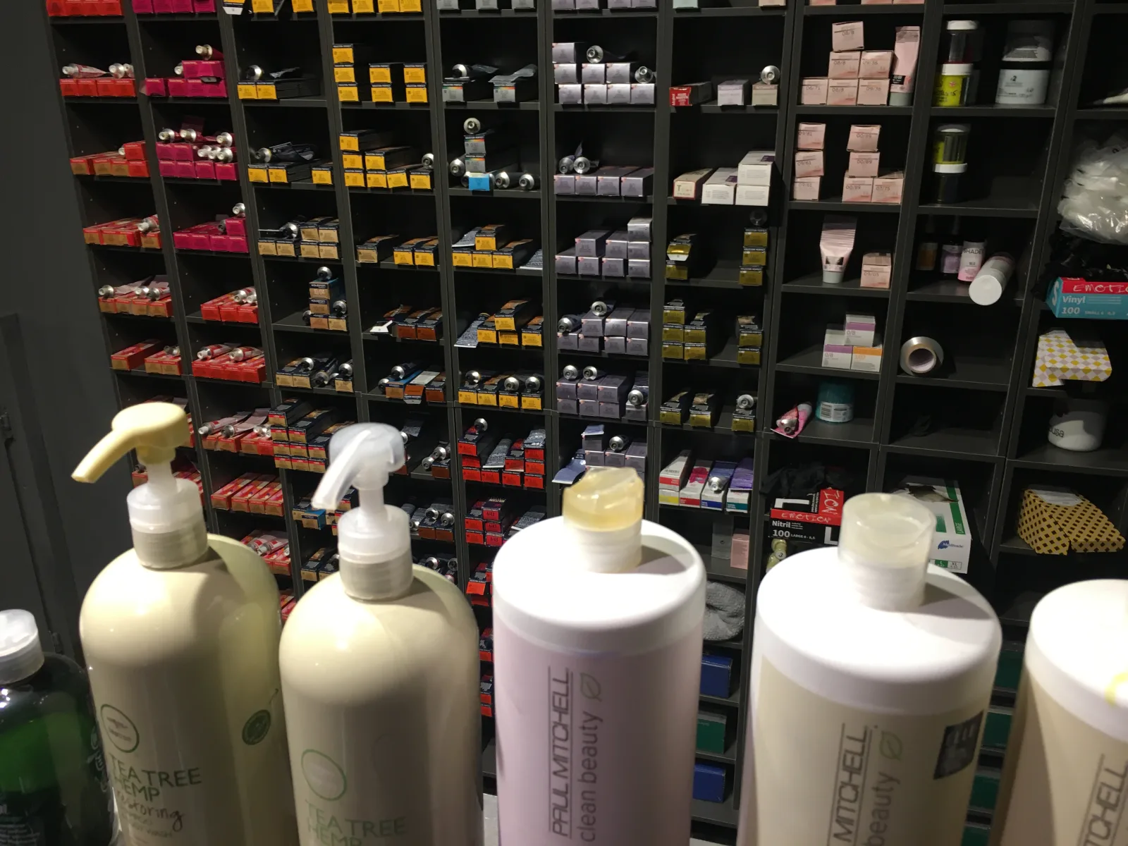 Hair care products in liter bottles at a workplace of a hair salon, in front of a shelf with hair dyes