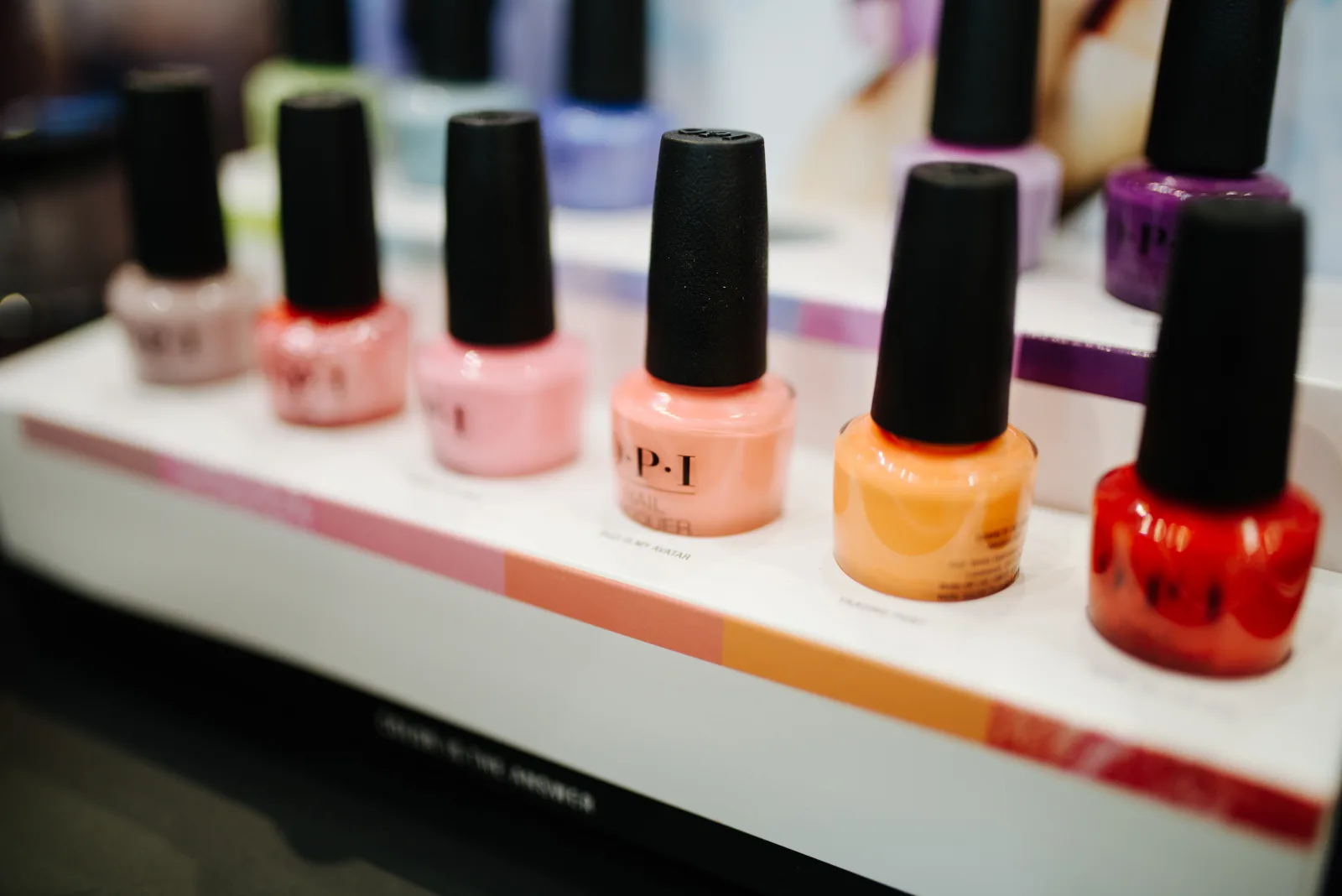 Vibrant nail polish bottles in various shades are neatly arranged on a shelf in a beauty salon. The display showcases an array of pastel and bold colors, creating an inviting atmosphere.