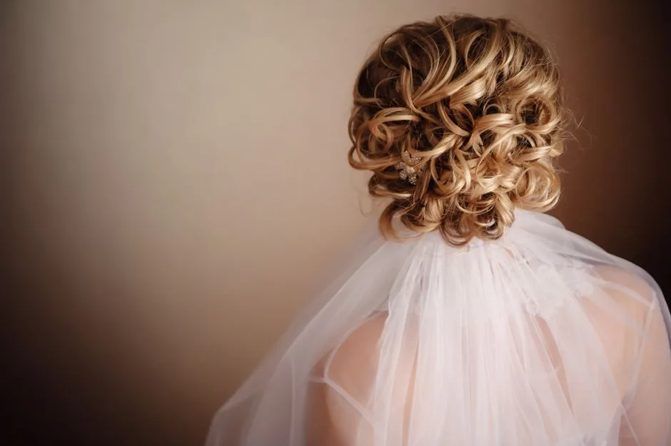 A beautiful bridal hairstyle featuring an elegant curly blonde updo accented with a white veil.