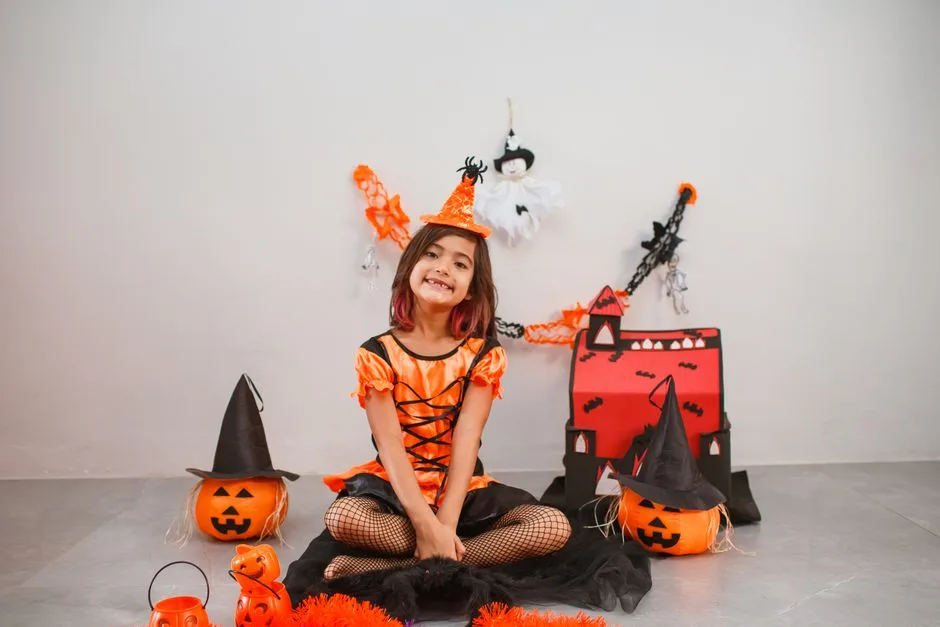 Cute child in a witch costume with Halloween decor, pumpkins, and festive backdrop.