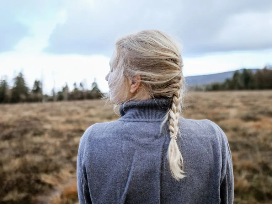Back view of woman with blonde braid standing in open nature. Ideal for relaxation themes.