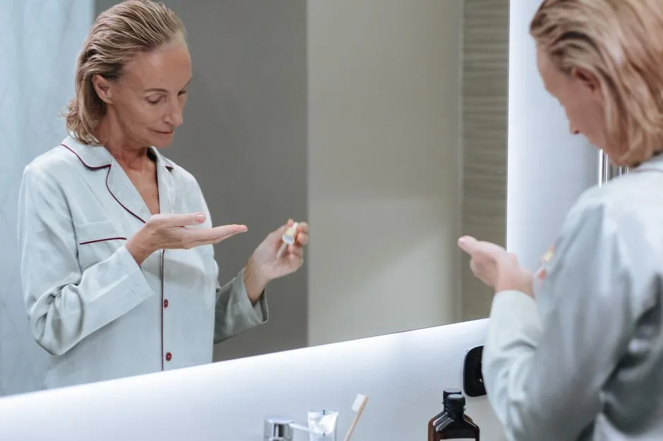 Senior woman applying skincare serum in front of bathroom mirror during her morning routine.