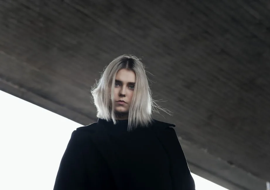 A low angle shot of a serious woman with platinum blonde hair under an urban bridge in Germany.