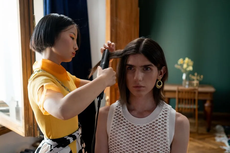 A hairdresser styling a client's hair with a flat iron in a contemporary salon setting.