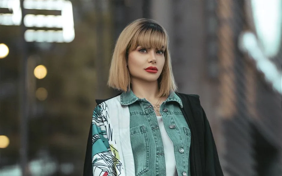 Portrait of a fashionable woman in a denim jacket with a blurred urban background.
