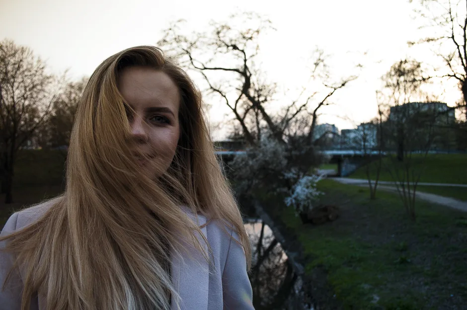 A serene portrait of a woman with blonde hair in a Warsaw city park during dusk.