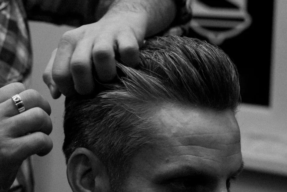 Barber styling a man's hair in a Moscow salon, captured in grayscale.