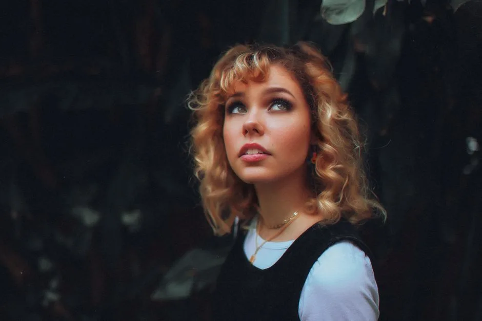 Blond woman with curly hair gazing upwards in a dark background portrait.