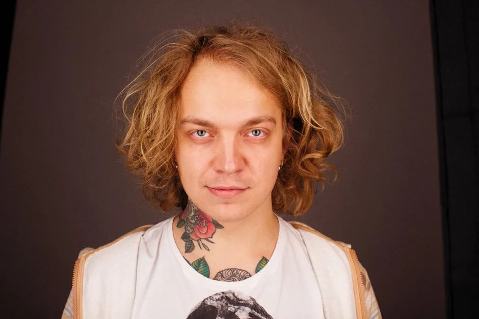 Portrait of a tattooed man with long curly hair and a relaxed expression.