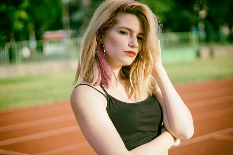 Confident young woman with blonde hair posing on an outdoor running track, enjoying the summer day.