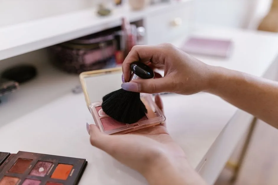 Close-up of woman's hands applying blush with a brush, indoors.