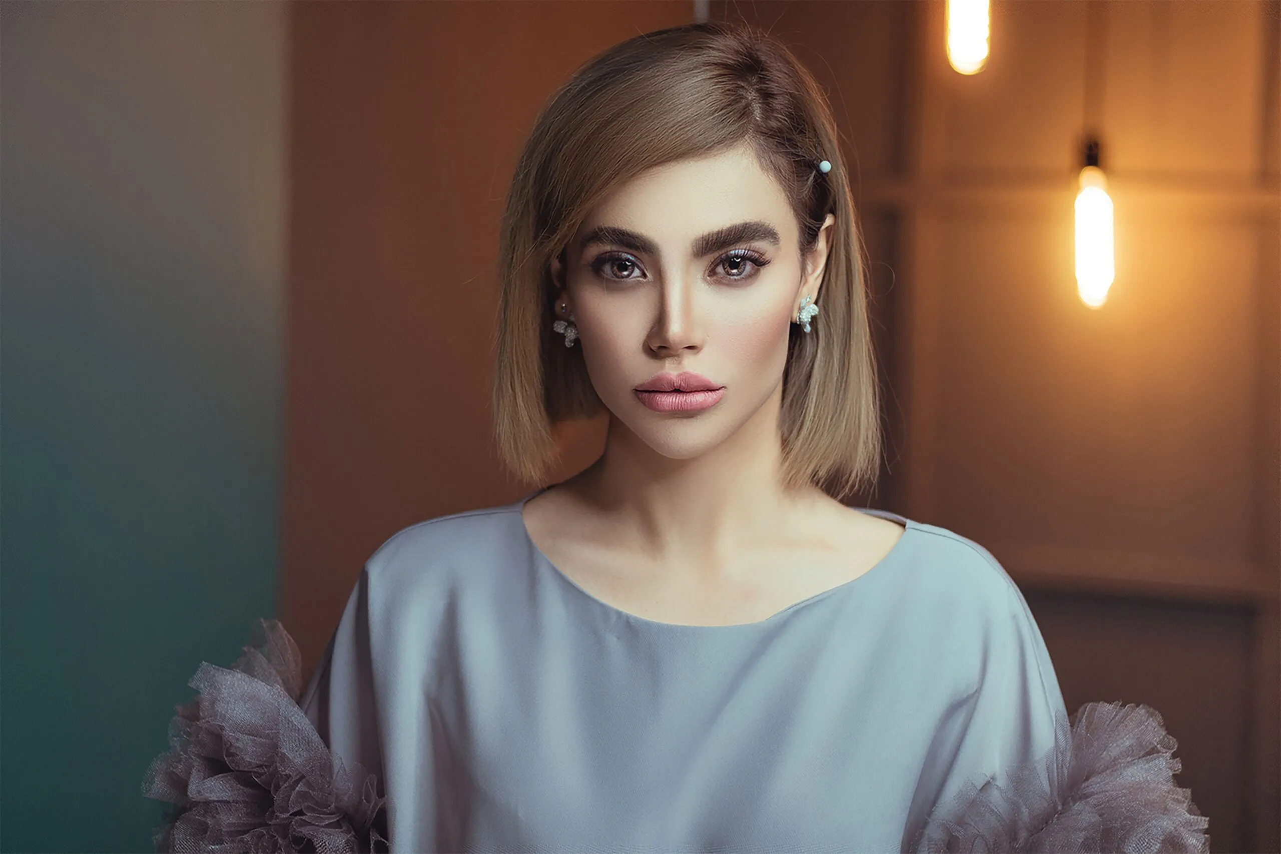 A sophisticated portrait of a woman indoors with modern lighting, featuring elegant attire and makeup.