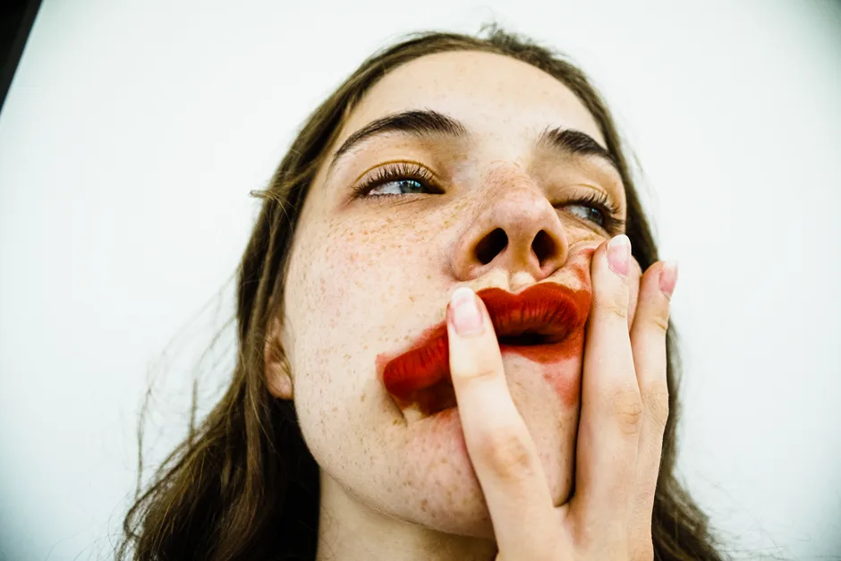 Artistic close-up of a person with smudged red lipstick and noticeable freckles, creating a striking visual.
