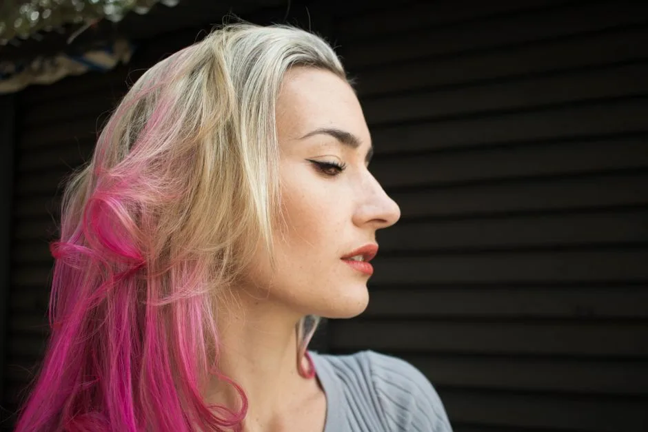 Profile of a fashionable woman with blonde and pink hair in an outdoor setting.