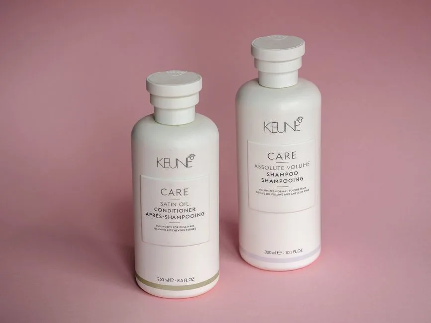 White Keune shampoo and conditioner bottles on a soft pink background.