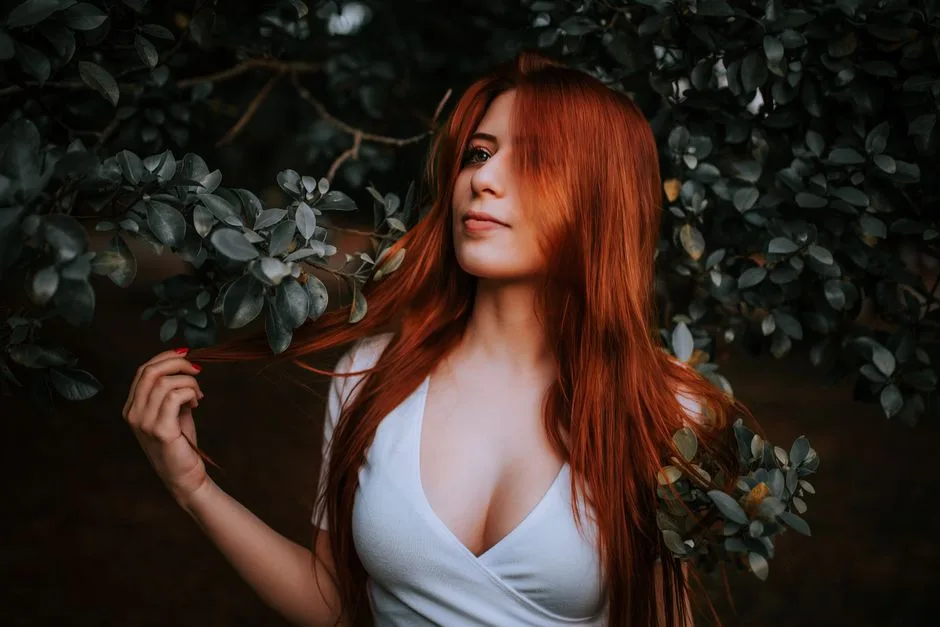 Close-up portrait of a red-haired woman surrounded by greenery, embodying natural beauty.