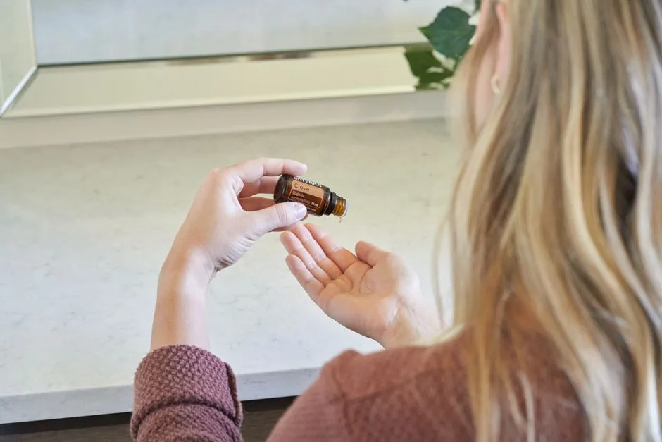 Back view of a woman applying clove essential oil with natural light in a bathroom setting.