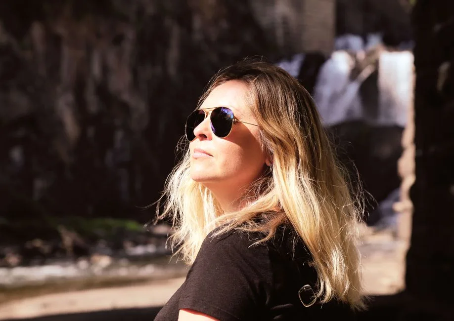 Blonde woman with sunglasses enjoying a sunny day by a waterfall.