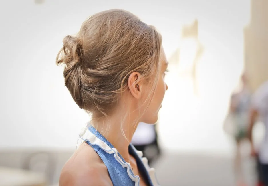 Side view of a woman with blonde hair styled in an updo, against a blurred indoor background.