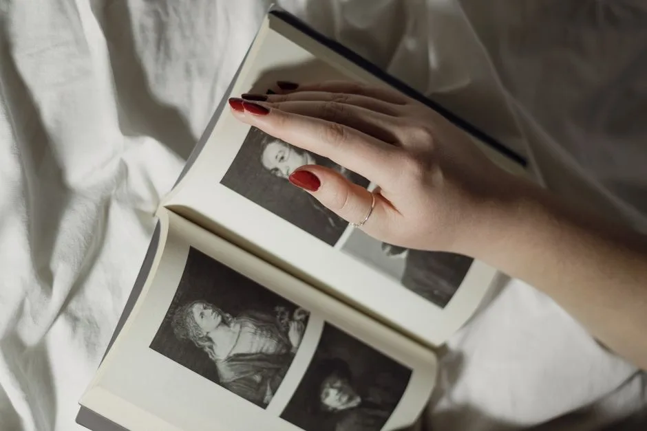 A woman's hand with red nails rests on a vintage photo book, showcasing black and white portraits.