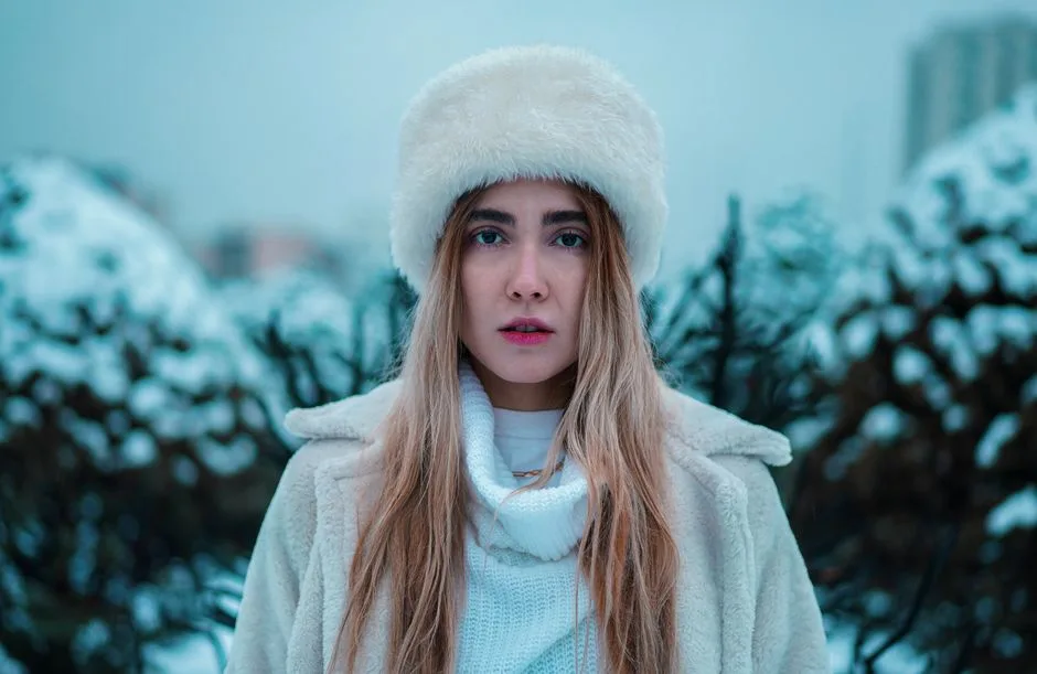 Portrait of a woman in winter attire with a fur hat, white coat, and blonde hair outdoors.