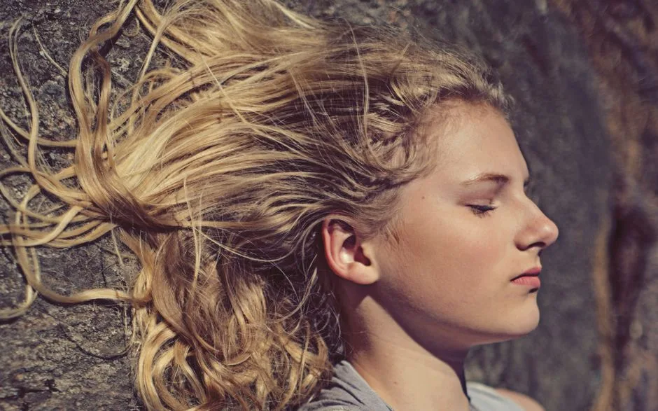 Close-up portrait of a young woman with flowing blonde hair in natural light.