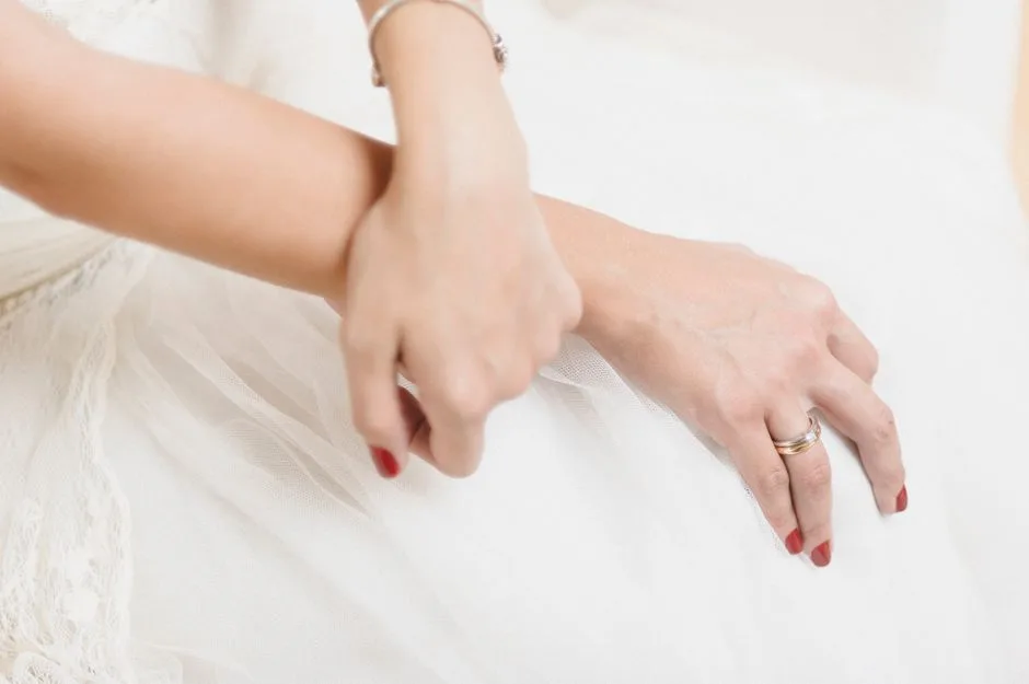 Close-up image showcasing elegant hands with red nails, a wedding ring, and jewelry.