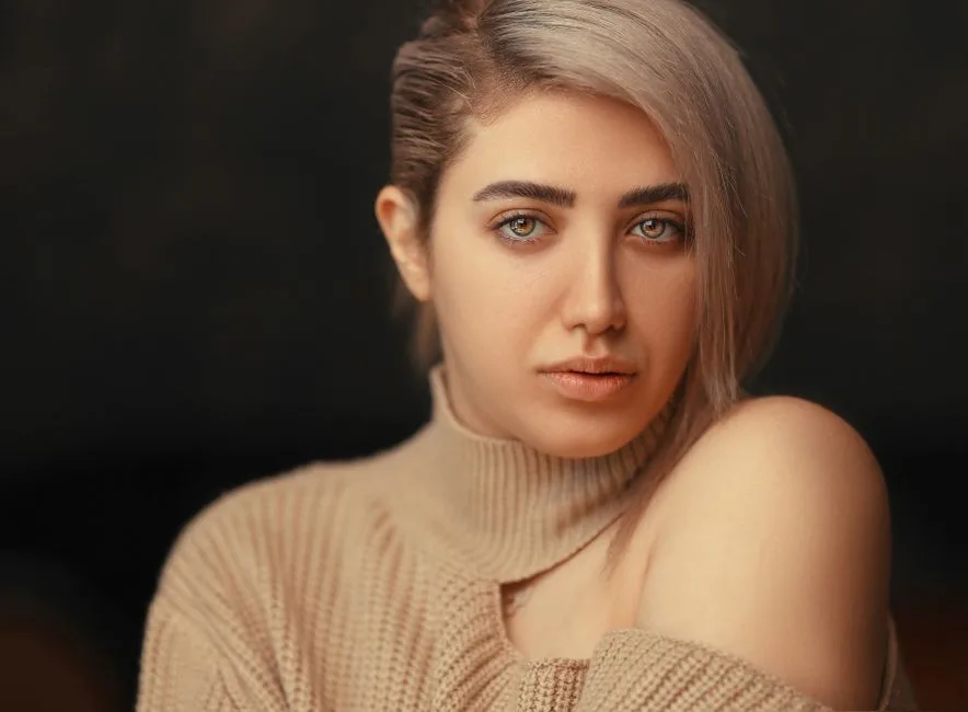 Studio portrait of a woman wearing a beige sweater, showcasing a stylish modern look.