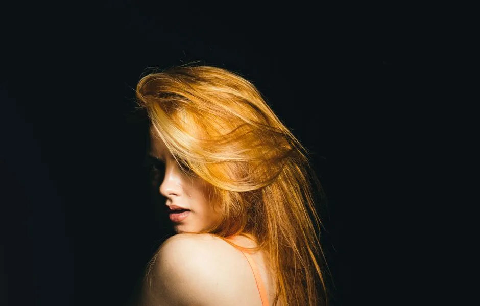Elegant portrait of a red-haired woman with long flowing hair against a dramatic black background.