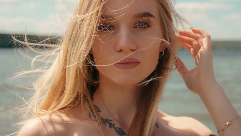 Blonde woman with tattoos enjoying a breezy day by the lake, captured in a fashion portrait.
