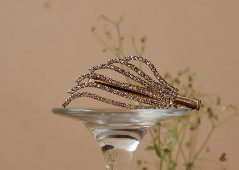 A close-up of a diamond-studded gold hair clip elegantly displayed on a glass against a soft brown background.