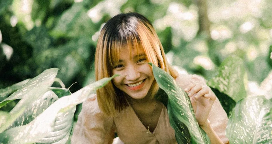 A woman smiling amid vibrant green leaves, enjoying nature's beauty.