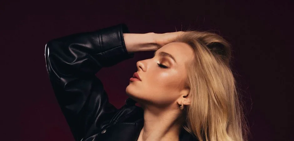 A beautiful young blonde woman poses gracefully with eyes closed, exuding elegance and style.