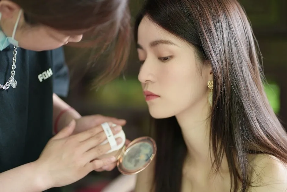 A makeup artist carefully applies powder to a young woman's face, highlighting natural beauty.