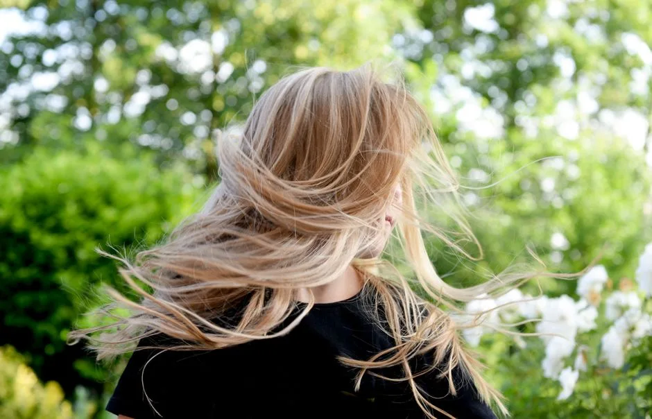 Blonde woman outside with hair blowing in the wind on a sunny summer day.