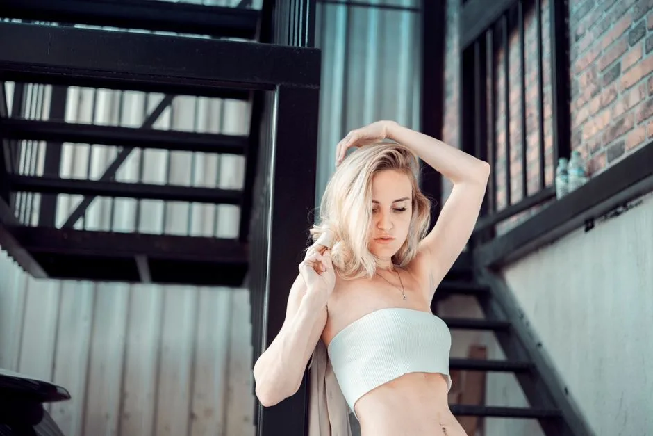 Chic fashion portrait of a woman with blonde hair, posing by an industrial staircase.