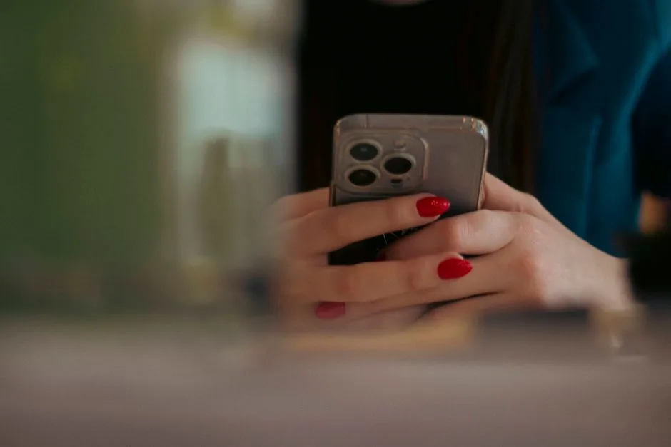 Close-up shot of a woman texting on a smartphone indoors, showcasing red nail polish.
