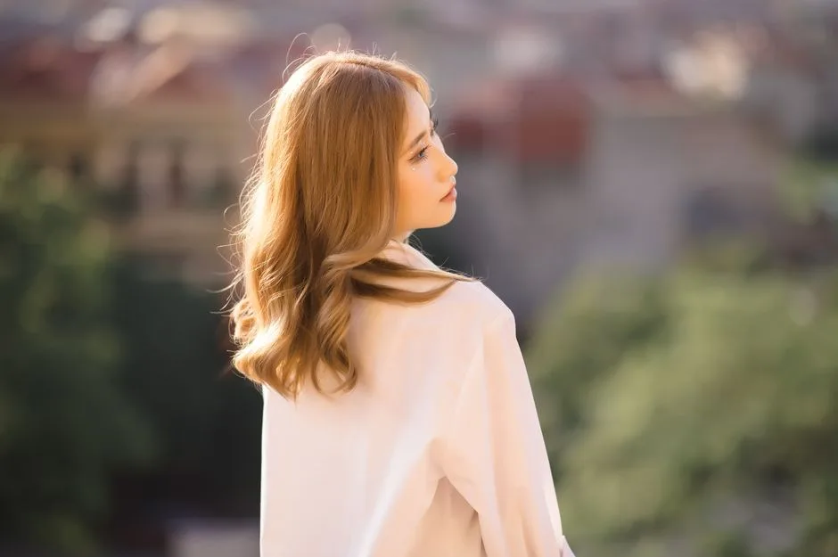 A reflective young woman looking over an urban backdrop, bathed in soft sunlight.
