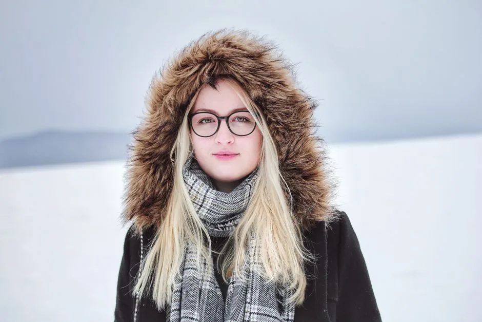 Portrait of a young woman outdoors in winter, wearing glasses and a fur-lined hooded coat.