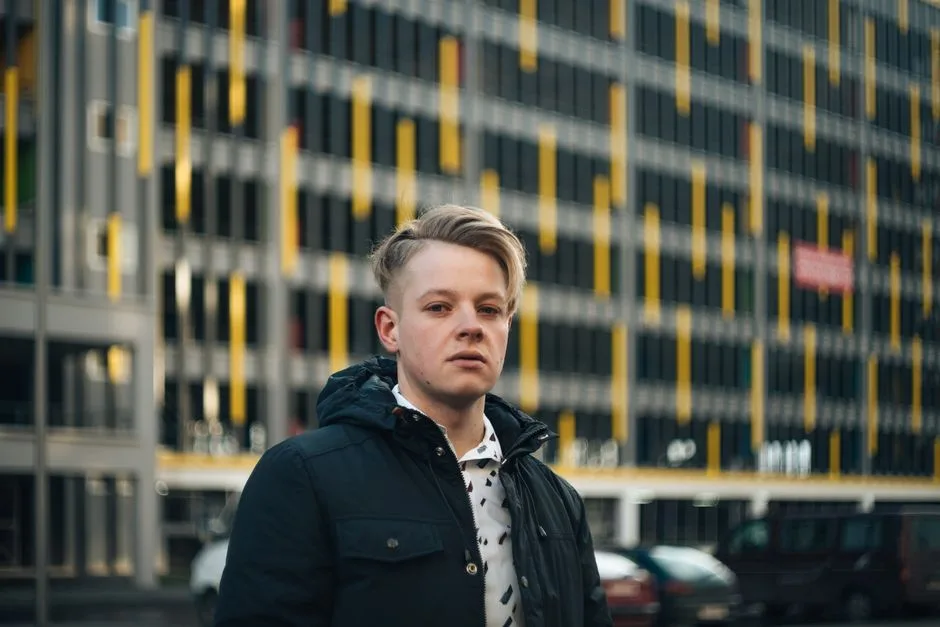 Stylish man with blonde hair in urban setting, wearing a dark jacket.