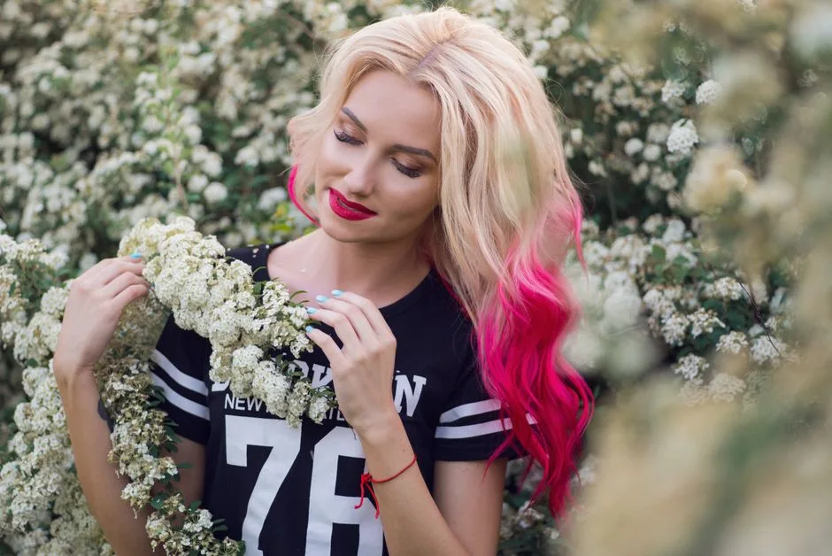 A beautiful woman with vibrant hair stands among blooming white flowers, creating a serene summer portrait.