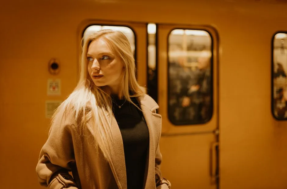 Stylish woman with blonde hair posing in a subway station, showcasing urban fashion.