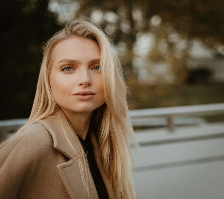 Stylish blonde woman posing outdoors in autumn attire with a serene smile.