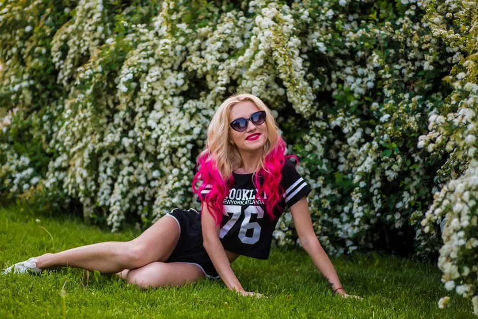 Woman with pink hair enjoying a sunny day outdoors in a blossoming garden.