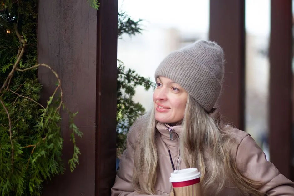 Blonde woman outdoors in winter, holding a coffee cup, wearing a coat and beanie.