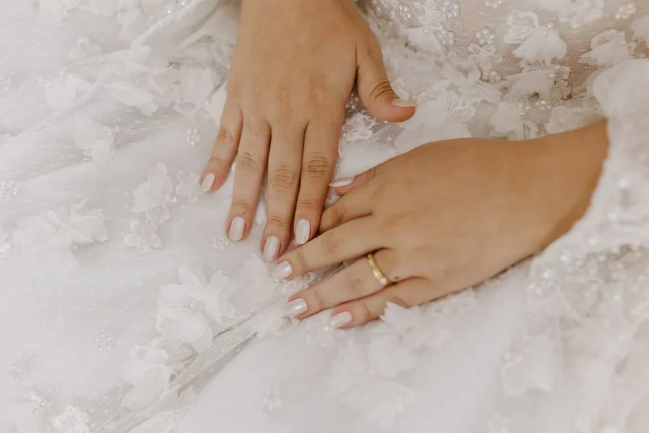 Close-up of a bride's hands with delicate lace detailing and a wedding ring on a beautiful wedding dress.