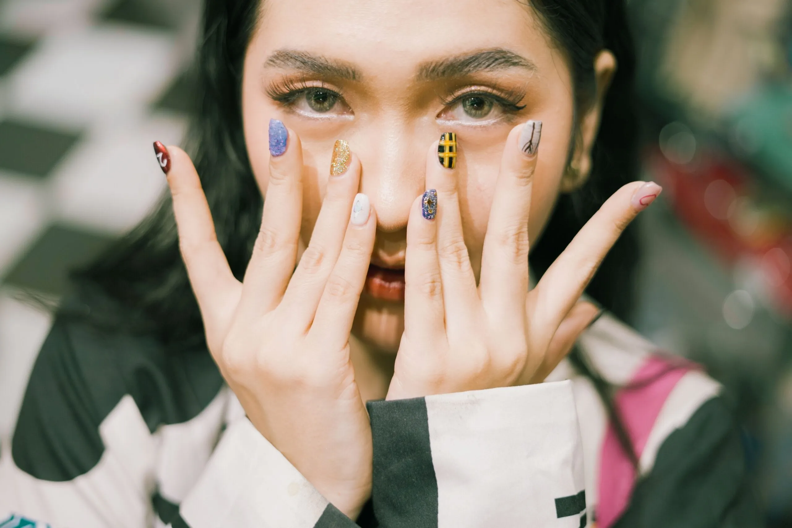 Close-up shot of a woman with colorful acrylic nails covering her face.