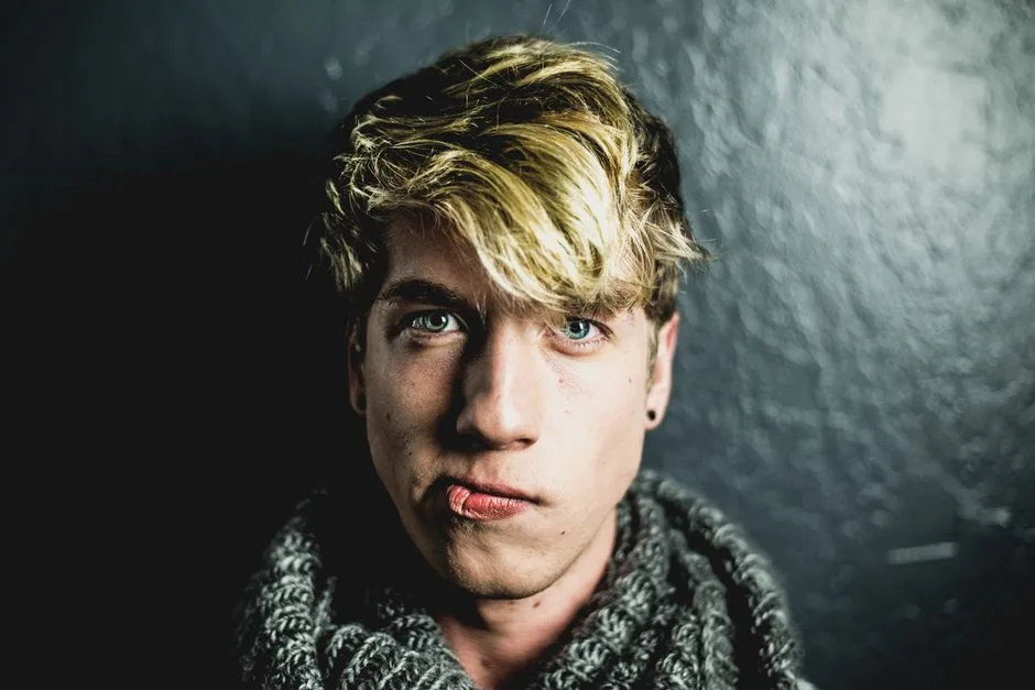 Portrait of a young man with blonde hair wearing a scarf against a dark background.
