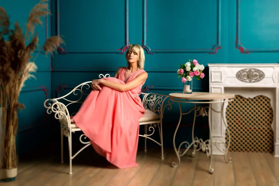 A woman in a pink gown relaxes on a bench in a stylish, vintage room.