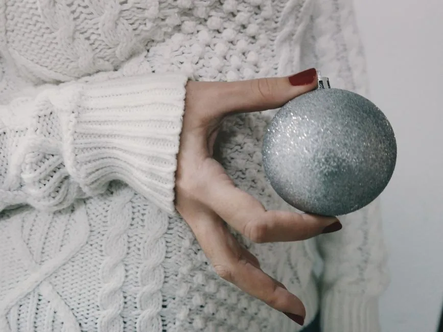 Close-up of a woman holding a glittery Christmas ball, wearing a cozy knit sweater.